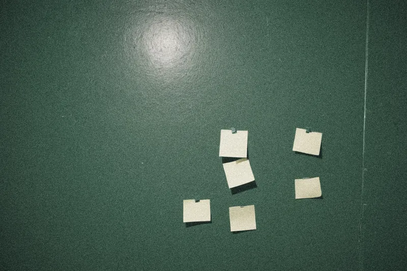 Notas adhesivas amarillas, en blanco, pegadas torcidas en una pared verde oscura