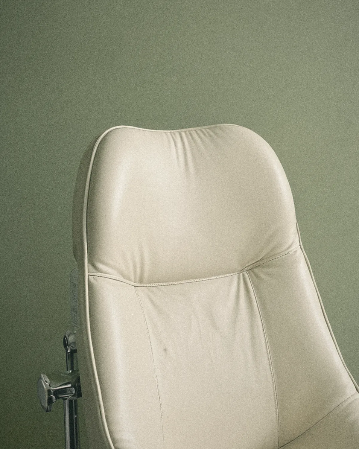 Respaldo de un sillón dental de vinilo marfil bajo una lámpara desenfocada
