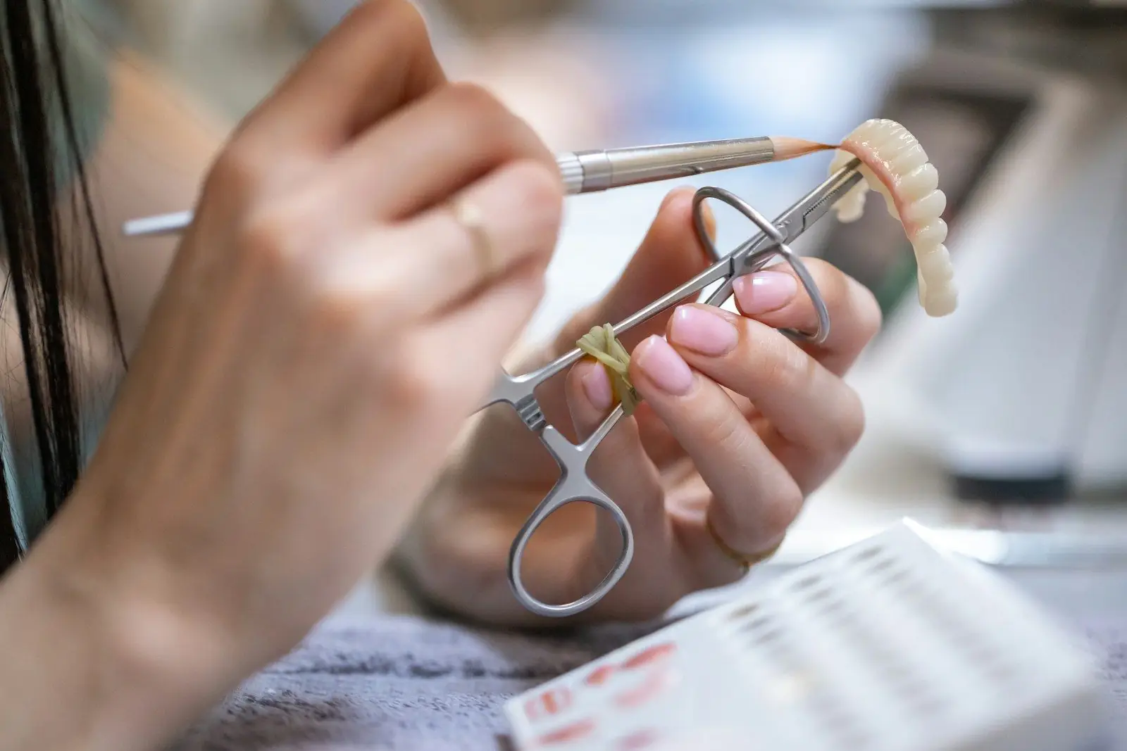 Manos trabajando una prótesis dental con pinzas