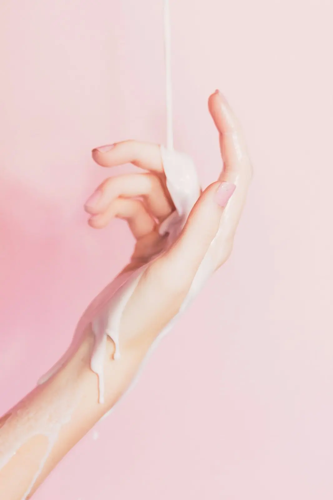 Mano bajo un hilo de leche sobre fondo rosa