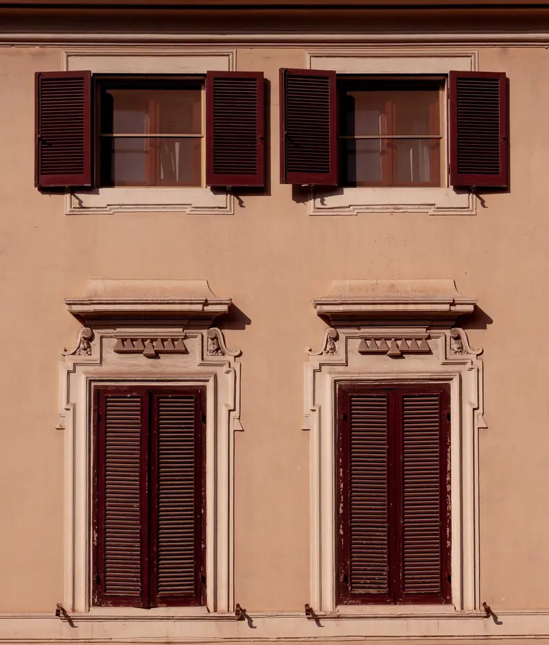 Dos balcones con postigos de madera granate en una fachada color arcilla