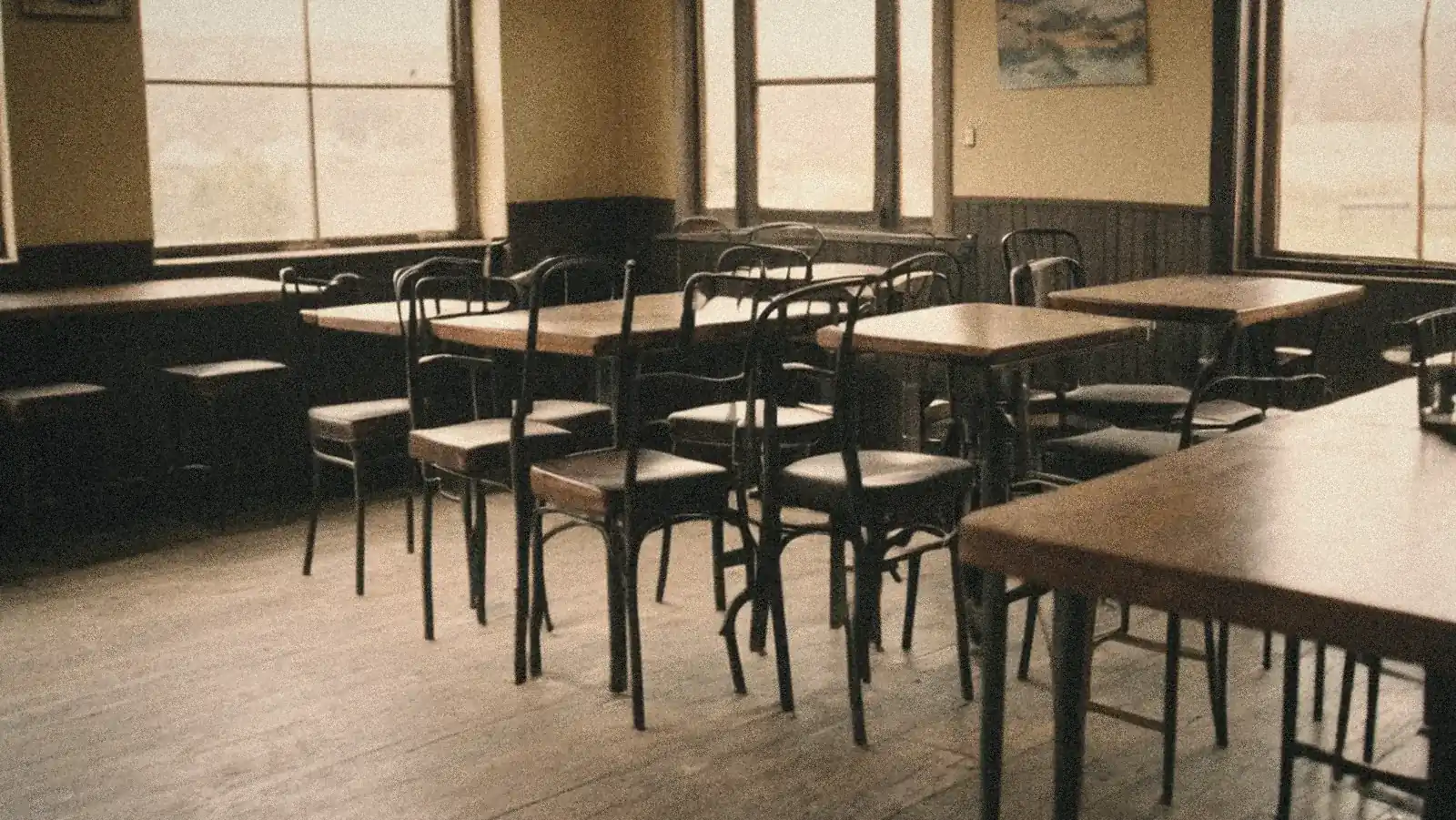 Un bar vacío por la mañana, con las sillas en su sitio y la luz fría de la ventana (imagen generada con IA)